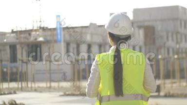 一个年轻的女建筑工人站在施工现场并控制工作<strong>流程</strong>的背面<strong>视图</strong>。